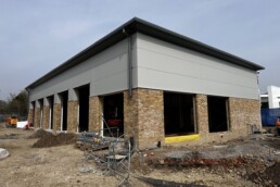 Current exterior construction progress of the whole building including the Formula One Autocentres unit, showing the modern structural framework and new cladding being installed on the commercial unit.