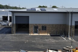 Current exterior construction progress of Unit 2, showing the roller shutter door, glazed window and pedestrian door, and EV charger on the commercial unit.
