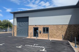 Completed exterior of Unit 2 at Broad Oak Business Park showing the installed roller shutter, glazed entrance, 3 parking spaces and EV charger.